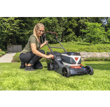 Frau bedient einen Rasenmäher im Garten.