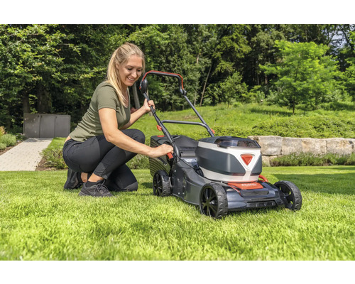 Frau bedient einen Rasenmäher im Garten.