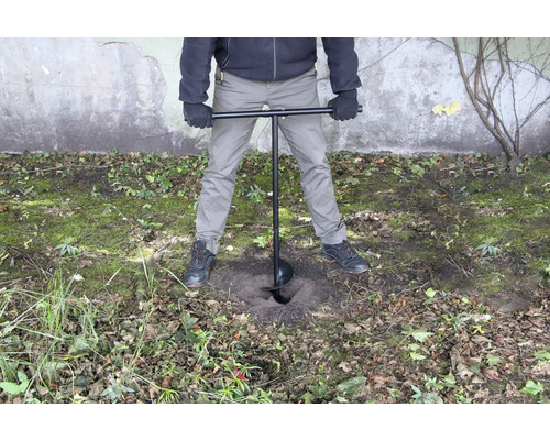 Eine Person verwendet einen Erdbohrer, um ein Loch in den Boden zu bohren.