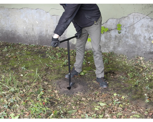 Eine Person bohrt mit einem Erdbohrer ein Loch in den Boden.