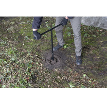 Eine Person benutzt einen Erdbohrer, um ein Loch in den Boden zu bohren.