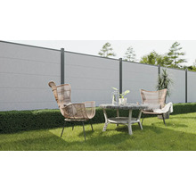 Gartenszene mit Betonzaun, Rattansesseln und rundem Tisch auf einer Rasenfläche.