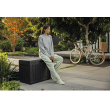 Szene im Garten mit einer sitzenden Person auf einer Aufbewahrungsbox und einem Fahrrad im Hintergrund