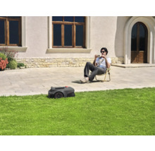 Ein Rasenmähroboter mäht den Rasen, während eine Person im Garten sitzt.