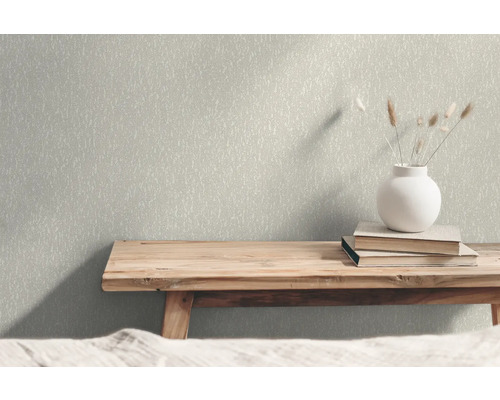Nahaufnahme einer Wand mit gemusterter Tapete, auf der sich eine Holzbank, Bücher und eine Vase befinden.