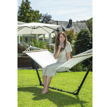 Frau sitzt in einer freistehenden Hängematte im Garten und trinkt ein Getränk.