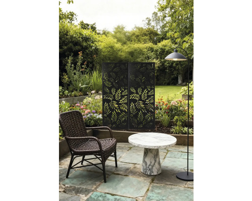 Gartenszene mit Rattan-Sessel, Marmortisch, Stehlampe und Sichtschutz mit Blätterdesign.