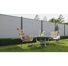 Gartenszene mit Betonzaun, zwei Rattansesseln und einem runden Tisch auf einer Rasenfläche.