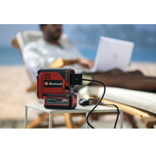 Einhell Akku-Lampe mit USB-Anschluss auf einem Tisch, im Hintergrund eine Person mit Laptop