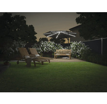 Garten mit Liegestühlen, Bank und beleuchtetem Sonnenschirm bei Dämmerung