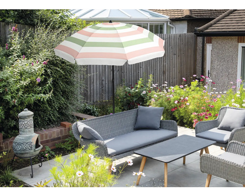 Gartenszene mit Sitzgruppe aus Rattan, Sonnenschirm mit Streifenmuster, Blumen und Chiminea.