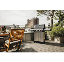 Edelstahl Grill auf einer Dachterrasse neben einem Holztisch und Stühlen.