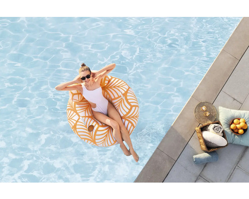Frau entspannt sich auf einem Schwimmring im Pool, mit Handtüchern und Getränken am Beckenrand