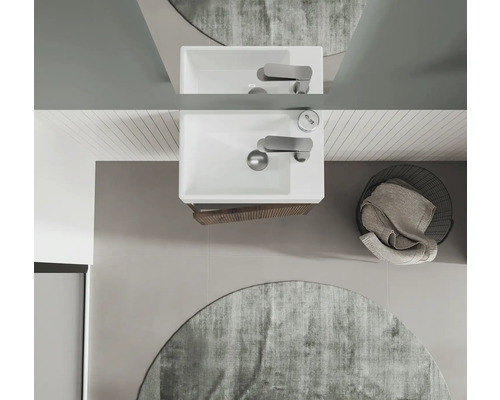 Draufsicht eines Badezimmers mit Waschbecken, Armatur, Spiegel, rundem Teppich und Wäschekorb