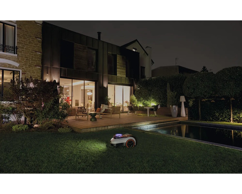 Rasenmähroboter bei der Nachtarbeit in einem Garten mit Haus und Pool.