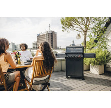 Personen sitzen auf einer Dachterrasse am Tisch und grillen mit einem Gasgrill.