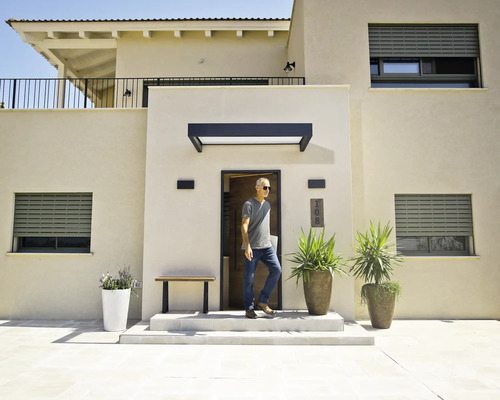 Modernes Haus mit hellen Fassaden, grauen Rolläden, einem schwarzen Vordach über der Haustür und großen Pflanzgefäßen im Eingangsbereich.
