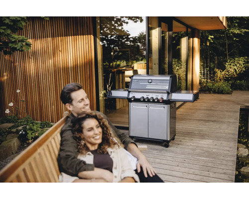 Paar entspannt auf einer Bank im Freien mit einem Gasgrill im Hintergrund.