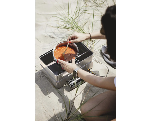 Person kocht Eintopf auf einem Gaskocher im Freien.