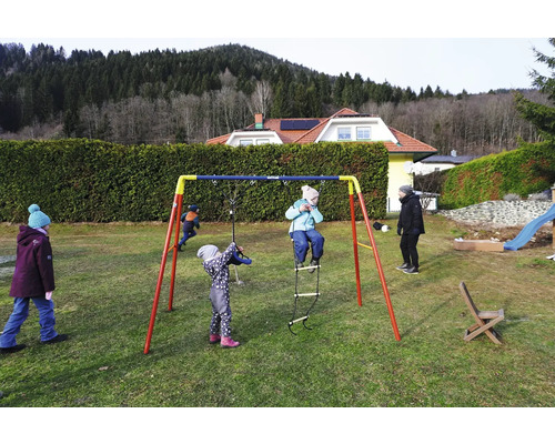 Kinder spielen auf einem Kettler Schaukelgerüst im Garten.