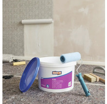 Szene mit einem Eimer Vliestapetenkleister, einer Farbwalze, einer Tapetenbürste und einer angefangenen Tapete an der Wand