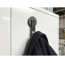 Schwarzer magnetischer Kleiderhaken an einer weißen Oberfläche mit aufgehängter Jacke