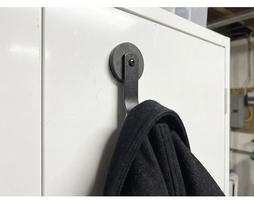 Schwarzer magnetischer Kleiderhaken an einer weißen Oberfläche mit aufgehängter Jacke