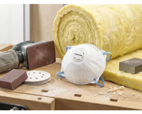 Szene mit Staubschutzmaske, Schleifpapier, Schleifmaschine und Dämmwolle auf einer Werkbank.