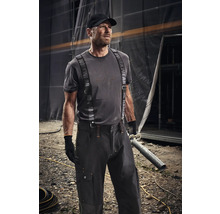 Mann in Arbeitskleidung mit Hosenträgern und Mütze hält ein Rohr