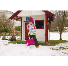 Mädchen schaufelt Schnee vor einem Spielhaus im Garten