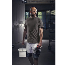 Handwerker mit T-Shirt, Shorts, Eimer und Glättkelle auf einer Baustelle.