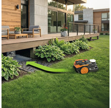 Rasenmähroboter fährt unter eine Holzterrasse mit einer grünen Richtungspfeilmarkierung.