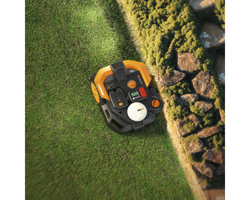 Aufsicht eines Mähroboters auf Rasen neben einer Steinmauer