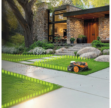 Ein Rasenmähroboter mäht den Rasen vor einem modernen Haus mit Steinfassade und großem Garten.