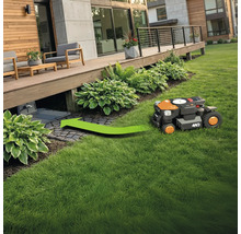 Ein Rasenmähroboter fährt auf einer Rasenfläche in Richtung Ladestation.