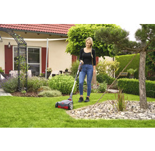 Frau benutzt Rasenlüfter im Garten vor dem Haus.