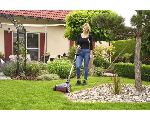 Frau benutzt Rasenlüfter im Garten vor dem Haus.