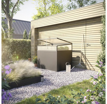 Gartenszene mit einem Pflanztisch aus Metall mit transparenter Abdeckung, einer Gießkanne und einem Rechen vor einer Holzwand.