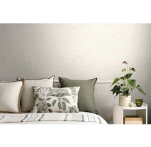 Bett mit Dekokissen, geripptem Kopfteil und weißem Beistelltisch mit Pflanze vor einer hellen Wand in einem modernen Schlafzimmer.