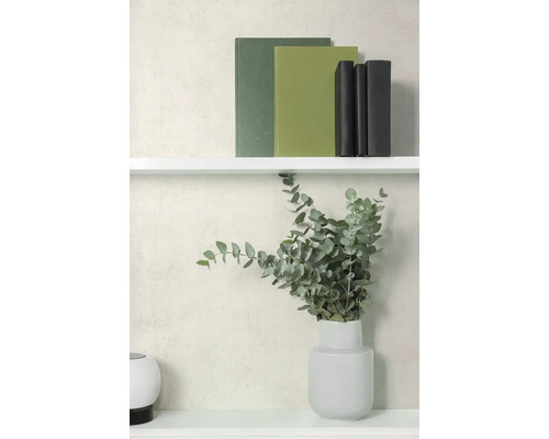 Vliestapete mit dezenter Struktur in hellem Beige hinter einem weißen Regal mit Büchern und einer Vase mit Eukalyptuszweigen.