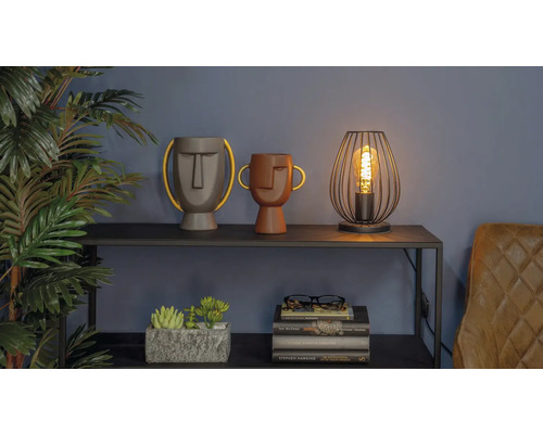 Dekorative Szene mit zwei Vasen mit Gesichtern, einer Lampe und einem Bücherstapel auf einem Regal.