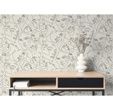 Moderne Tapete mit schwarzen Line-Art-Gesichtern hinter einem Holzschreibtisch mit weißer Vase und Trockenblumen in einem hellen Zimmer.