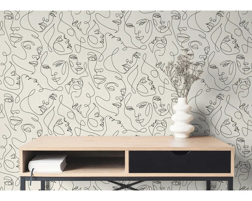 Moderne Tapete mit schwarzen Line-Art-Gesichtern hinter einem Holzschreibtisch mit weißer Vase und Trockenblumen in einem hellen Zimmer.