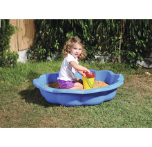 Mädchen spielt in einer blauen Sandmuschel mit Sandspielzeug im Garten.