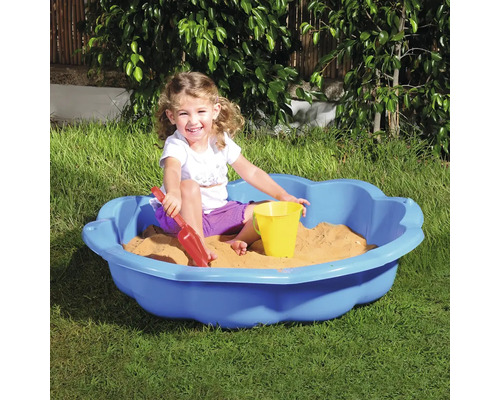 Kind spielt in einem blauen Sandkasten mit Sandspielzeug im Garten