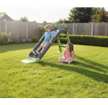 Junge rutscht auf einer Kinderrutsche im Garten, während ein Mädchen zusieht