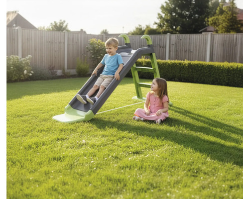 Junge rutscht auf einer Kinderrutsche im Garten, während ein Mädchen zusieht