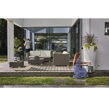 Helle, moderne Holzterrasse mit grauen Loungemöbeln aus Polyrattan, weißen Sitzkissen, Pflanzgefäßen und einer Gießkanne aus Metall.