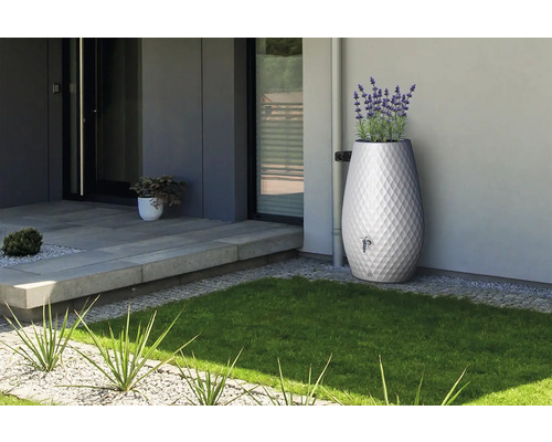 Dekorativer Regenspeicher in modernem Garten, rautenförmiges Oberflächenmuster, integrierter Pflanztopf mit Lavendel, Anschluss an Fallrohr.