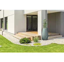 Dekorativer Regenspeicher und Pflanzkübel an einer Holzterrasse eines modernen Wohnhauses mit Garten und Rasenfläche.